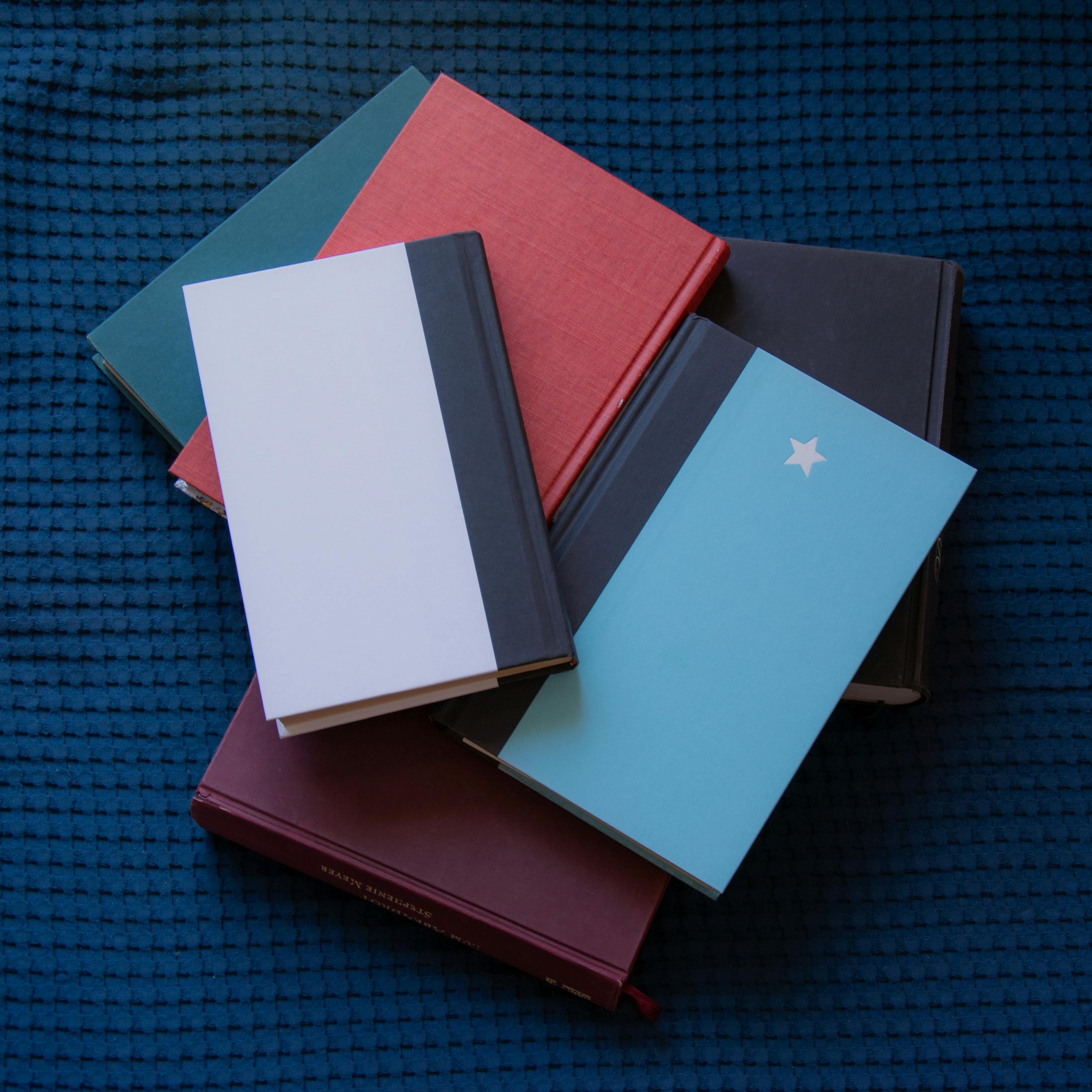 Books in various colors stacked on blue fabric, perfect for educational themes.